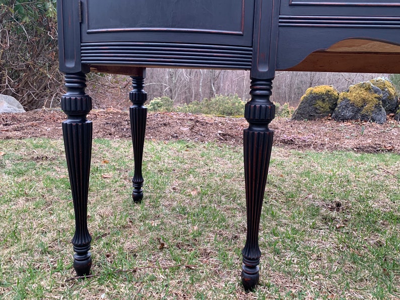 May include: Close-up of the black painted legs of a vintage buffet. The legs are turned and have a fluted design.