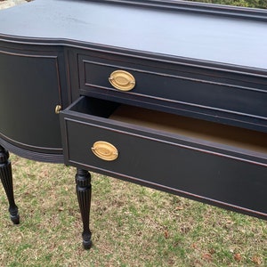 May include: Black painted wooden sideboard with three drawers and two cabinet doors. The sideboard has turned legs and brass hardware.