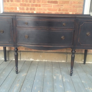 K&ouml;nnte beinhalten: Ein schwarzes Vintage-Buffet mit zwei T&uuml;ren und drei Schubladen. Das Buffet hat gedrehte Beine und ist mit einer dunkelbraunen Beize behandelt.