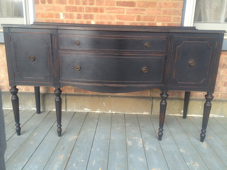 K&ouml;nnte beinhalten: Ein schwarzes Vintage-Buffet mit zwei T&uuml;ren und drei Schubladen. Das Buffet hat gedrehte Beine und ist mit einer dunkelbraunen Beize behandelt.