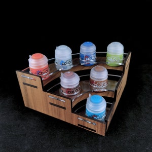Może przedstawiać: Drewniany stojak na pojemniki z farbą z siedmioma małymi pojemnikami. Pojemniki są oznaczone "Citadel Colour" i są w różnych kolorach, w tym niebieskim, czerwonym, brązowym i zielonym.