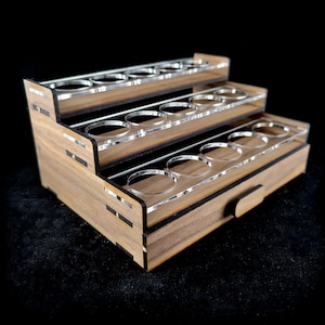 May include: A wooden paint rack with three tiers and a drawer. The rack has clear acrylic paint pot holders.