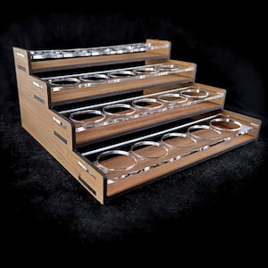 Puede incluir: Un estante de pintura de madera con cinco niveles, cada nivel tiene un estante de acrílico transparente con recortes circulares para sostener botellas de pintura. El estante está hecho de madera marrón claro con ribetes marrones oscuros.