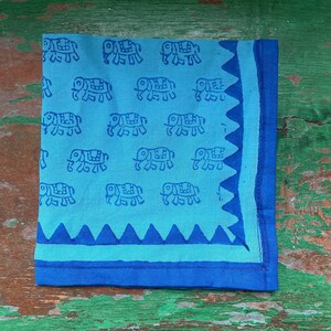 Puede incluir: Un pa&ntilde;uelo de algod&oacute;n azul con estampado de elefantes blancos y borde azul. El borde tiene un borde festoneado.