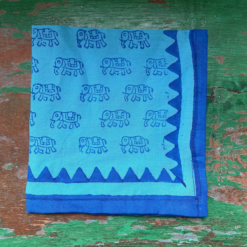 Puede incluir: Un pa&ntilde;uelo de algod&oacute;n azul con estampado de elefantes blancos y borde azul. El borde tiene un borde festoneado.