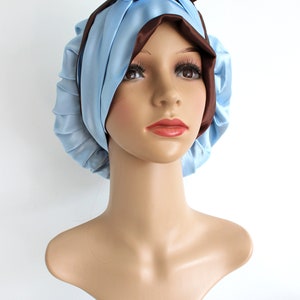 May include: A light blue satin sleep cap with a brown satin bow on top. The cap is designed to protect hair while sleeping.