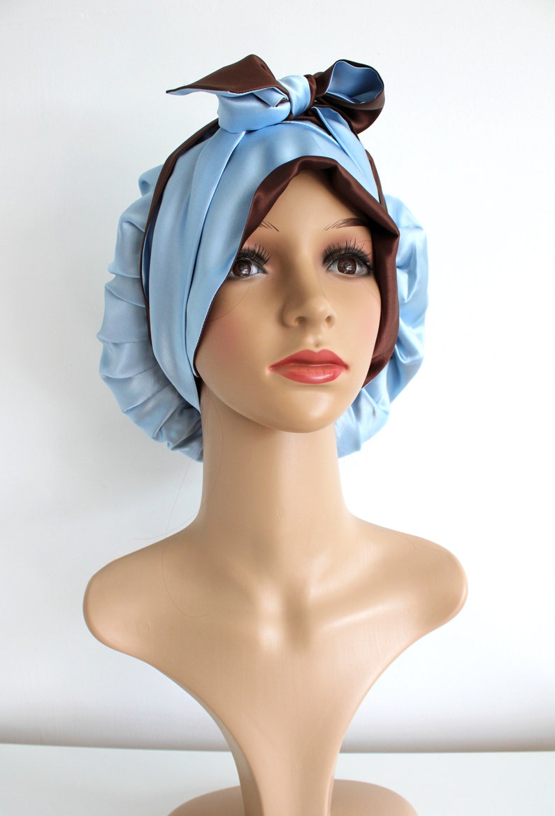 May include: A light blue satin sleep cap with a brown satin bow on top. The cap is designed to protect hair while sleeping.