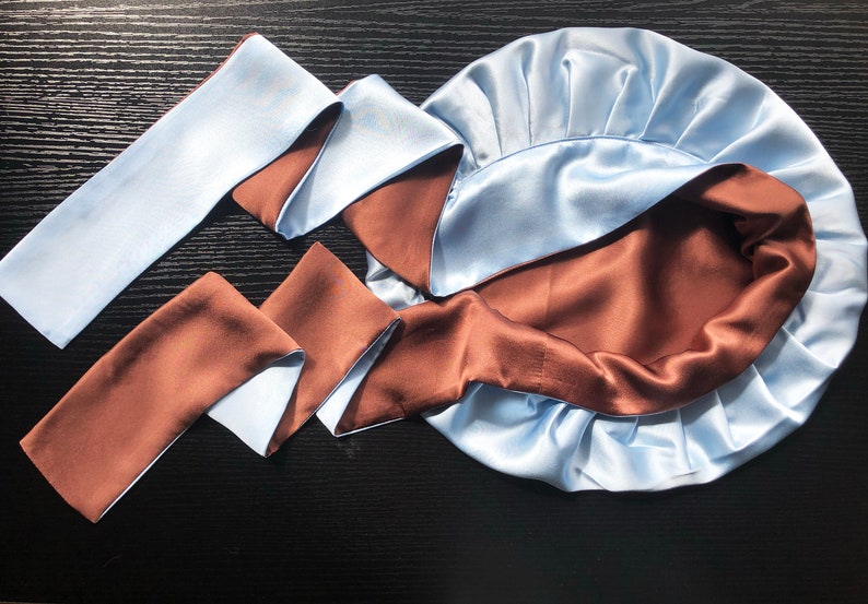 May include: A light blue satin sleep cap with a brown satin lining. The cap is tied with a long, reversible satin ribbon that is light blue on one side and brown on the other.