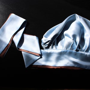 May include: A light blue satin sleep cap with a brown trim. The cap is folded in half and has a long, thin, light blue satin ribbon with a brown trim.