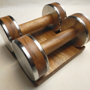 Puede incluir: Dos mancuernas de madera con detalles de acero inoxidable sobre una base de madera a juego. Las mancuernas tienen un acabado de veta de madera natural con bordes met&aacute;licos plateados. Dise&ntilde;adas para entrenamiento con pesas.