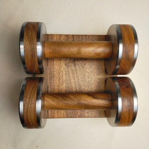 The Coretez dumbbell set, each weighing 6 kg, has smooth-textured wooden handles and stainless steel tips for an elegant look. They come with a matching wooden base for storage. Dumbbells add sophistication to any home gym.