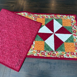 Pu&ograve; includere: Una trapunta fatta a mano con un retro a fantasia floreale rosso e un colorato design patchwork sul davanti. Il davanti presenta quadrati rossi, bianchi, verdi e arancioni, con un motivo a mulinello al centro. La trapunta misura circa 46 cm per 30 cm.