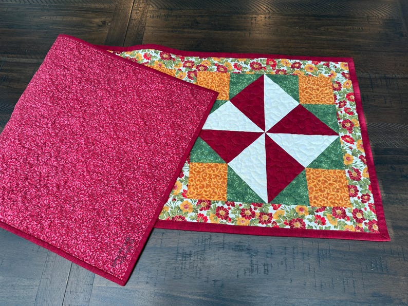 Pu&ograve; includere: Una trapunta fatta a mano con un retro a fantasia floreale rosso e un colorato design patchwork sul davanti. Il davanti presenta quadrati rossi, bianchi, verdi e arancioni, con un motivo a mulinello al centro. La trapunta misura circa 46 cm per 30 cm.