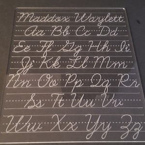 May include: A clear plastic dry-erase board with the alphabet written in cursive. The board is labeled "Maddox Wajlett" at the top.