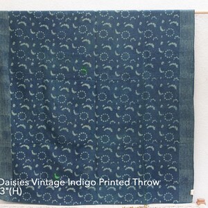 Op de afbeelding: Een blauwe en witte katoenen deken met een herhalend patroon van kleine cirkels en gebogen lijnen. De deken is 160 cm lang en 211 cm breed. "Dancing Daisies Vintage Indigo Printed Throw" is afgedrukt op de onderkant van de deken.