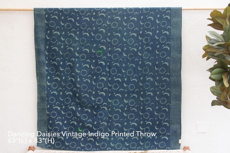 Op de afbeelding: Een blauwe en witte katoenen deken met een herhalend patroon van kleine cirkels en gebogen lijnen. De deken is 160 cm lang en 211 cm breed. "Dancing Daisies Vintage Indigo Printed Throw" is afgedrukt op de onderkant van de deken.