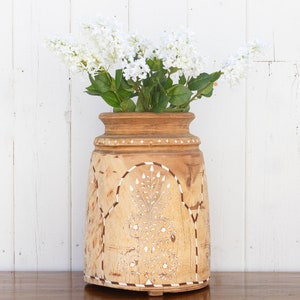 May include: A wooden vase with intricate carvings and a white floral design. The vase is filled with white flowers.