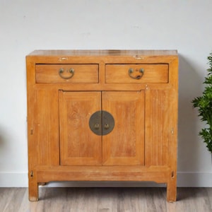May include: A wooden cabinet with two drawers and two doors. The cabinet is a light brown color and has brass hardware. The cabinet is sitting on a light brown floor.