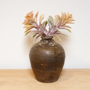 May include: A brown ceramic vase with a textured surface holds a cluster of dried, light pink and orange flowers.