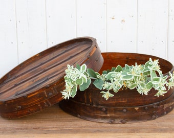 May include: Two round wooden boxes with a lid, one open and one closed. The boxes are brown and have a natural wood finish. The boxes are decorated with metal accents. A sprig of green and white flowers is placed on top of the boxes.