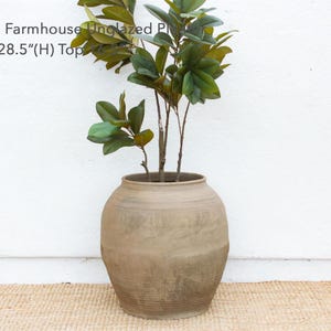 May include: An unglazed, oversized farmhouse planter, approximately 27 inches long and 28.5 inches high at the top, holds leafy green branches. The neutral-toned, textured pot sits on a woven mat against a white wall.