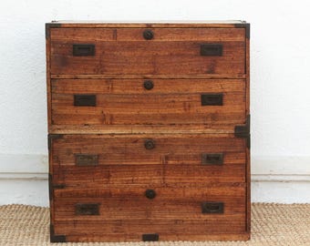 May include: A three-drawer wooden chest with a warm brown finish. The chest features metal hardware, including corner brackets, drawer pulls, and circular knobs. The wood grain is visible, adding to the rustic aesthetic.