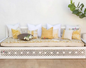 May include: White daybed with a lattice design and a white mattress. The daybed is decorated with yellow and white throw pillows. The daybed is in front of a white wall and a green plant in a white pot.