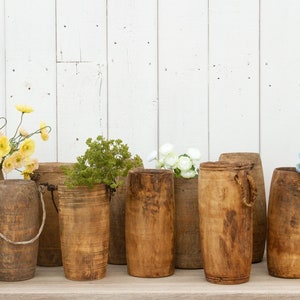 May include: A collection of wooden vases with various flowers, including yellow poppies, white flowers, and blue hydrangeas. The vases are all made of natural wood and have a rustic look.