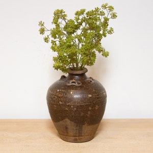 May include: A brown ceramic vase with a textured surface and a small opening at the top. The vase is filled with a bouquet of green flowers.
