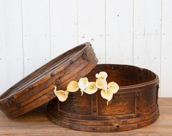 May include: A round wooden box with a lid, featuring a rustic brown finish and metal accents. The box is open, revealing a white wooden interior and a bouquet of white calla lilies.