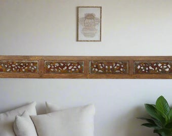 May include: A long, rectangular wooden wall panel with four carved floral designs. The panel is a warm brown color with hints of gold and white. A framed artwork hangs above the panel. The piece is likely a decorative element for home decor.