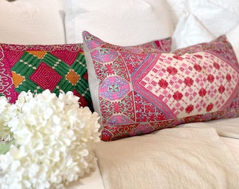 May include: Two decorative throw pillows with intricate embroidered patterns in shades of pink, green, and white. The pillows are arranged on a light beige fabric surface.
