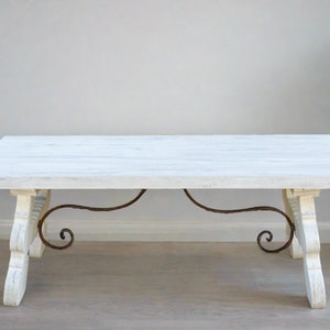 May include: White wooden coffee table with a distressed finish and ornate iron scrollwork accents. The table has a rectangular top and a simple, elegant design.