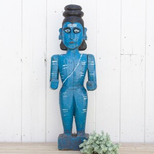 May include: A blue wooden statue of a Hindu deity with a black hair bun and white markings. The statue is standing on a wooden base.