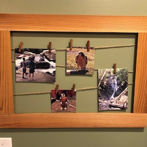 May include: A wooden picture frame with a rope and clothespins holding up four photos. The photos show a waterfall, a hawk, and two people standing in front of a waterfall.