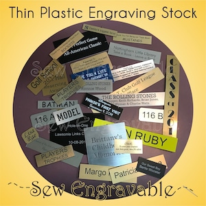 May include: A collection of thin plastic engraving stock in various shapes and colors, with engraved text. The text includes names, dates, and phrases like "Perfect Game" and "Players Trophies". The image is set against a dark purple background.