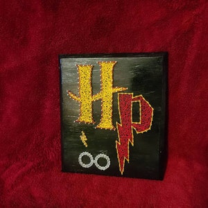 May include: A black wooden sign with string art depicting the Harry Potter symbol, "HP", with a lightning bolt and the Deathly Hallows symbol.