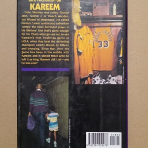 May include: A black and white photo of a man and a young boy walking down a hallway. The man is wearing a striped sweater and the boy is wearing a striped shirt. The text on the book cover reads "Jack Nicholson on Kareem".