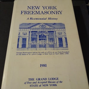 Puede incluir: Un libro blanco con texto azul que dice "New York Freemasonry: A Bicentennial History". La portada del libro presenta una ilustraci&oacute;n de un edificio con un grupo de personas frente a &eacute;l. El texto debajo de la ilustraci&oacute;n dice "George Washington tomando su juramento de cargo como nuestro primer presidente en la Biblia de la logia de San Juan en Nueva York el 30 de abril de 1789." El a&ntilde;o 1981 est&aacute; impreso debajo del texto. La parte inferior de la portada dice "The Grand Lodge of Free and Accepted Masons of the State of New York."