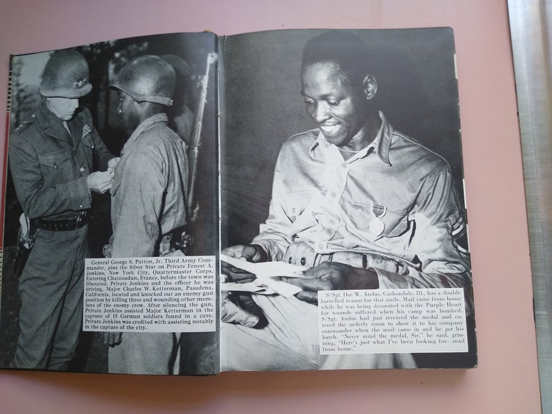 May include: A black and white photograph of a military officer pinning a medal on a soldier's uniform. The soldier is smiling and holding a letter. The text in the image reads: "Sgt. The W. Andrus, Carbonale, Ill., has a double barreled reason for that smile. Mail came from home while he was being decorated with the Purple Heart for wounds suffered just when his camp was bombed. Sgt. Andrus had got to remove it to his lonely room to show it to the company commander when the mail came in. He got his lunch. "Never mind the medal, Sir," he said, grinning. "Here's just what I've been looking for - mail from home."