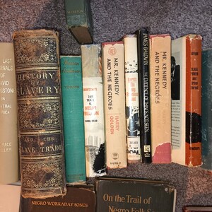 Puede incluir: Una estanter&iacute;a llena de libros sobre historia y la experiencia afroamericana. Los libros son principalmente marrones, negros y verdes con letras doradas. Algunos de los t&iacute;tulos incluyen "Historia de la esclavitud", "La evidencia de las cosas no vistas" y "El Sr. Kennedy y los negros".
