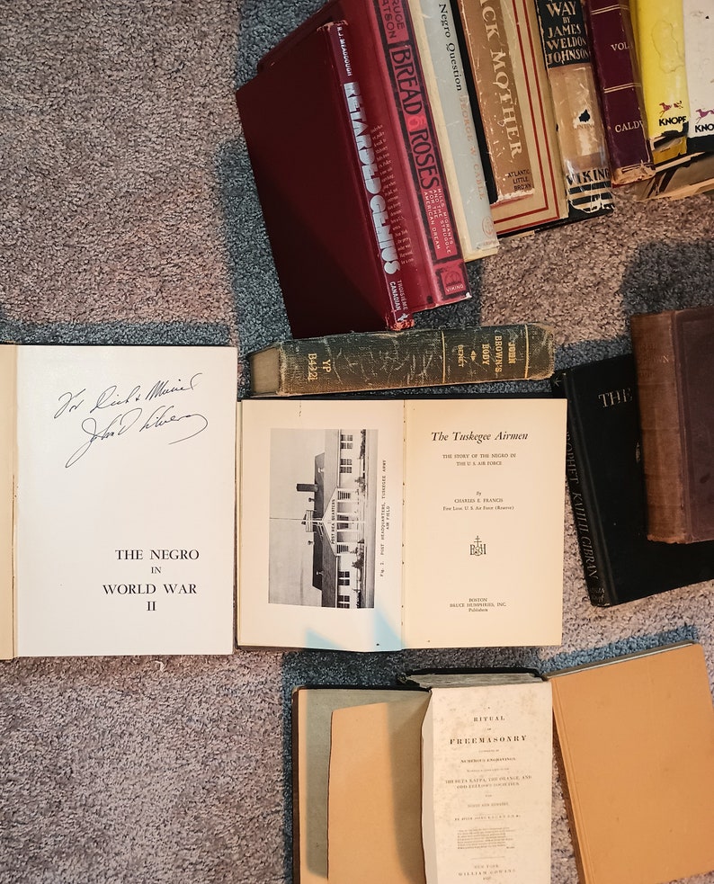 Puede incluir: Una colecci&oacute;n de libros antiguos con varios t&iacute;tulos, incluyendo "Bread Roses", "Black Mother", "The Negro in World War II" y "The Tuskegee Airmen". Los libros est&aacute;n dispuestos sobre una alfombra marr&oacute;n.