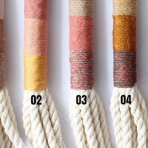 May include: Eight macrame plant hangers with different coloured yarn accents. The hangers are made of natural cotton rope and have a silver metal ring at the top. The colours of the yarn accents are beige, yellow, pink, red, grey, and brown.