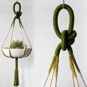 May include: A green and white macrame plant hanger with a white ceramic pot. The hanger is made of thick rope and has a tassel at the bottom.