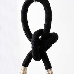Peut inclure: Une corde noire avec un nœud noué. La corde est suspendue à un crochet. La corde est attachée à une corde blanche.