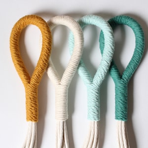 Peut inclure: Quatre suspensions macramé pour plantes dans différentes couleurs : jaune moutarde, blanc, bleu clair et sarcelle.