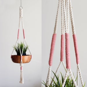 May include: A macrame plant hanger with a wooden bowl and pink accents. The hanger is made of white rope and has a pink tassel at the bottom.