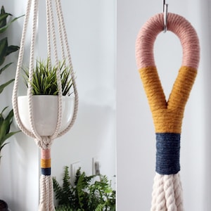 Puede incluir: Un macetero de macramé con una cuerda de algodón blanca y un acento rosa, amarillo y azul. El macetero sostiene una maceta de cerámica blanca con una planta verde.