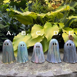 Puede incluir: Cinco figuras de fantasmas de cerámica con un acabado brillante. Cada fantasma tiene dos agujeros para los ojos y una forma drapeada y fluida. Los fantasmas son en tonos de azul, verde y rosa, con un aspecto texturizado. Están dispuestos sobre una superficie de piedra.
