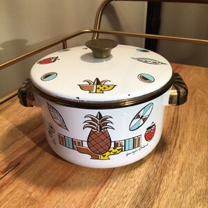 May include: White enamel pot with gold trim and a pineapple design. The pot has a lid with a gold knob and features a variety of colorful geometric patterns. The text "Georges Briard" is visible on the bottom of the pot.